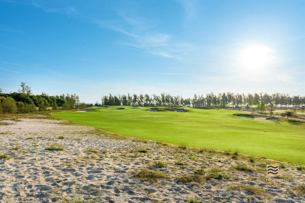 Wide fairway and native sand areas at Golden Sands Golf Resort near Hue, with the retained casuarina line separating the course from the sea