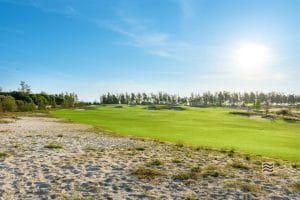Wide fairway and native sand areas at Golden Sands Golf Resort near Hue, with the retained casuarina line separating the course from the sea
