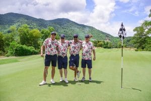 Four golfers in matching shirts on the green at a Central Vietnam golf course with mountains behind, the kind of society group that books a Da Nang golf trip from the UK