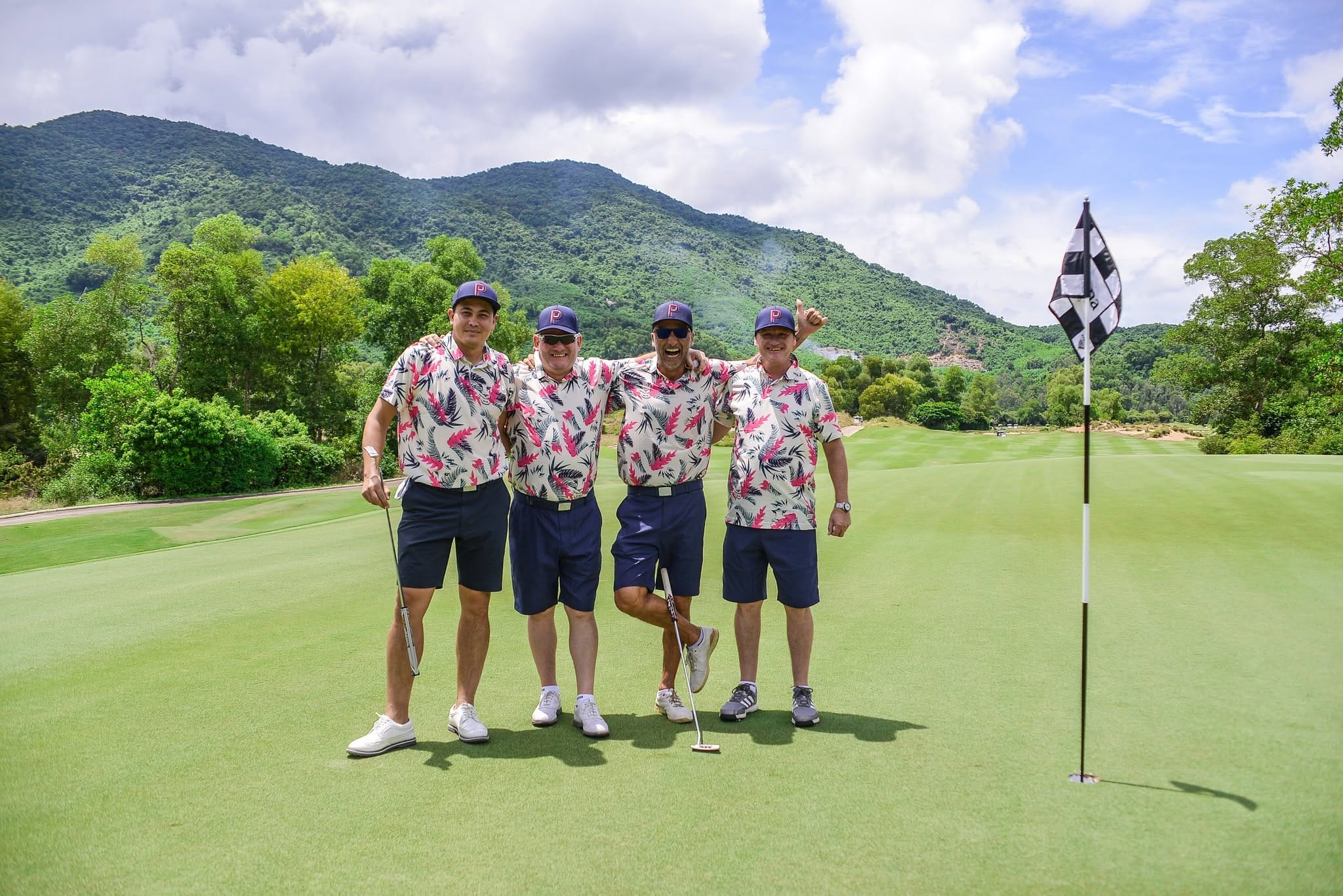 Four golfers in matching shirts on the green at a Central Vietnam golf course with mountains behind, the kind of society group that books a Da Nang golf trip from the UK