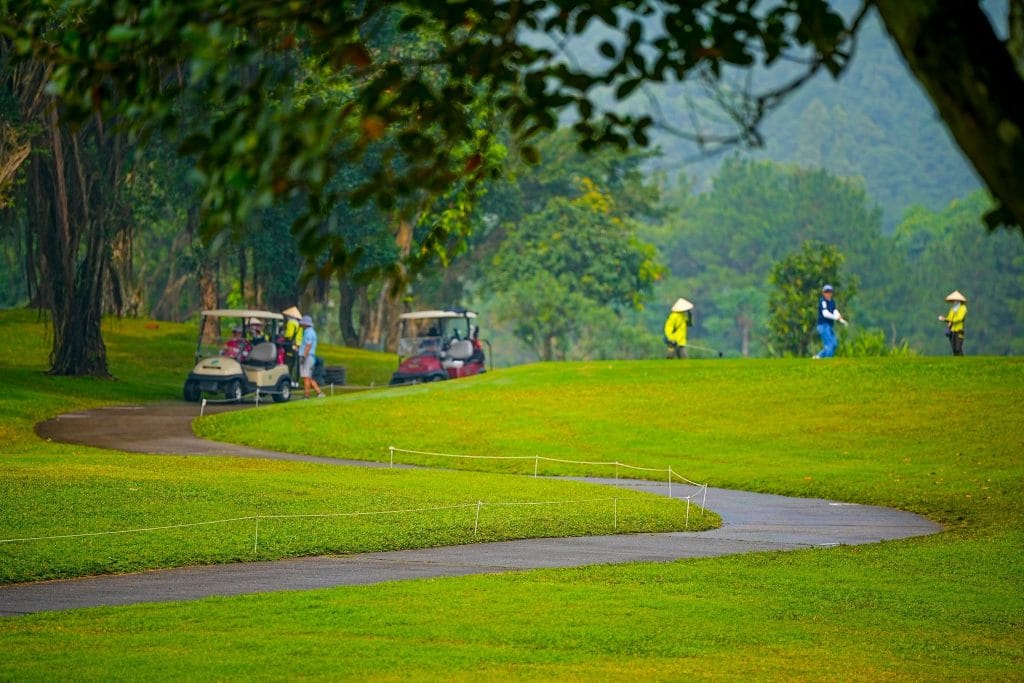Golfer and caddies walking the fairway at Tam Dao Golf Resort, with forested mountains in the mist behind