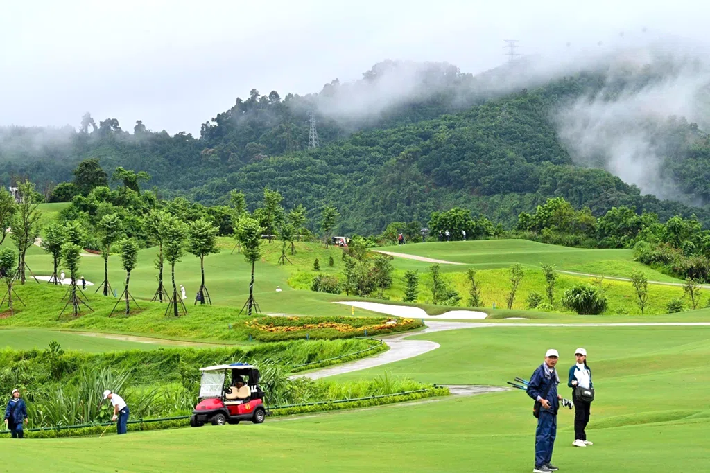 Morning fog clearing over a golf course near Hanoi in winter, with golfers and caddies on the fairway