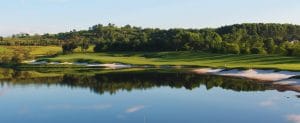 BRG Legend Hill Golf Resort green surrounded by sweeping sand bunkers, with a still lake reflecting the fairway at golden hour