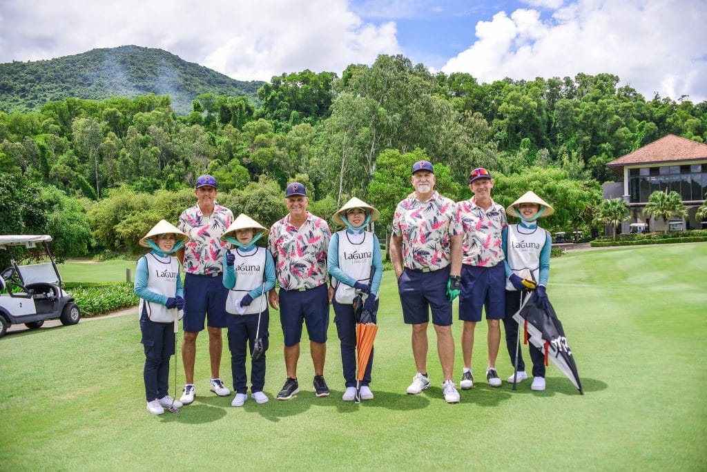 Four visiting golfers with their Vietnamese caddies in conical hats at Laguna Lang Co, central Vietnam — caddies are included in most Vietnamese green fees