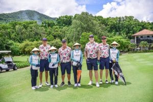 Four visiting golfers with their Vietnamese caddies in conical hats at Laguna Lang Co, central Vietnam — caddies are included in most Vietnamese green fees