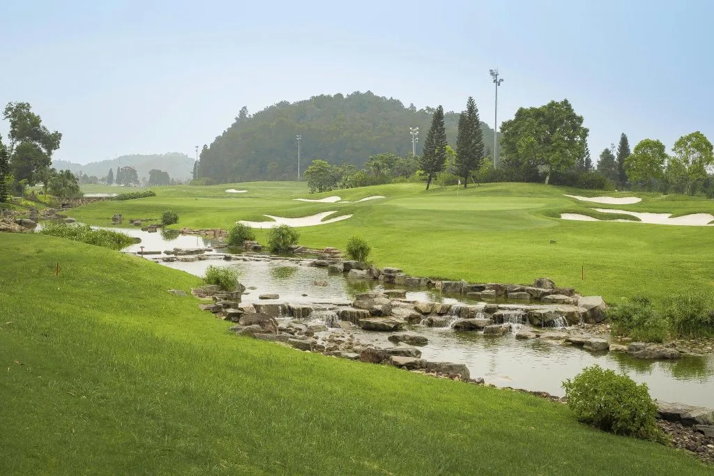 BRG Legend Hill Golf Resort green ringed by white sand bunkers with a stream at golden hour