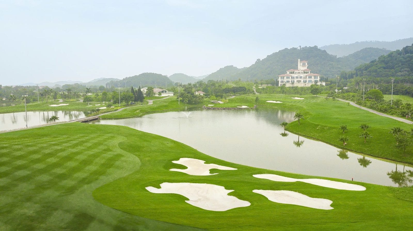 BRG Legend Hill Golf Resort fairway with white bunkers, a lake and the hilltop clubhouse in Soc Son near Noi Bai Airport