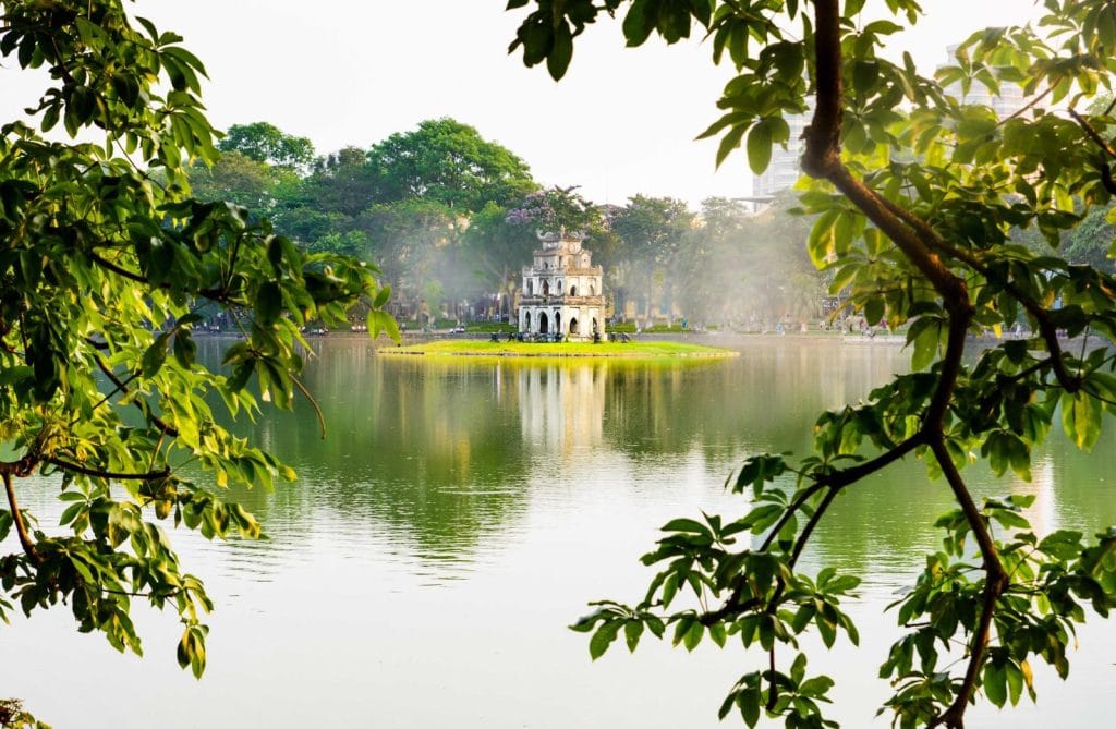 Turtle Tower on Hoan Kiem Lake framed by trees, a morning walk for non-golfers in Hanoi