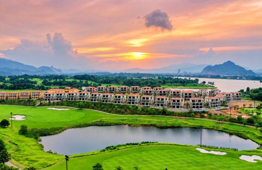 Golf resort villas beside a lake and fairway at sunset, a stay-and-play option near Hanoi