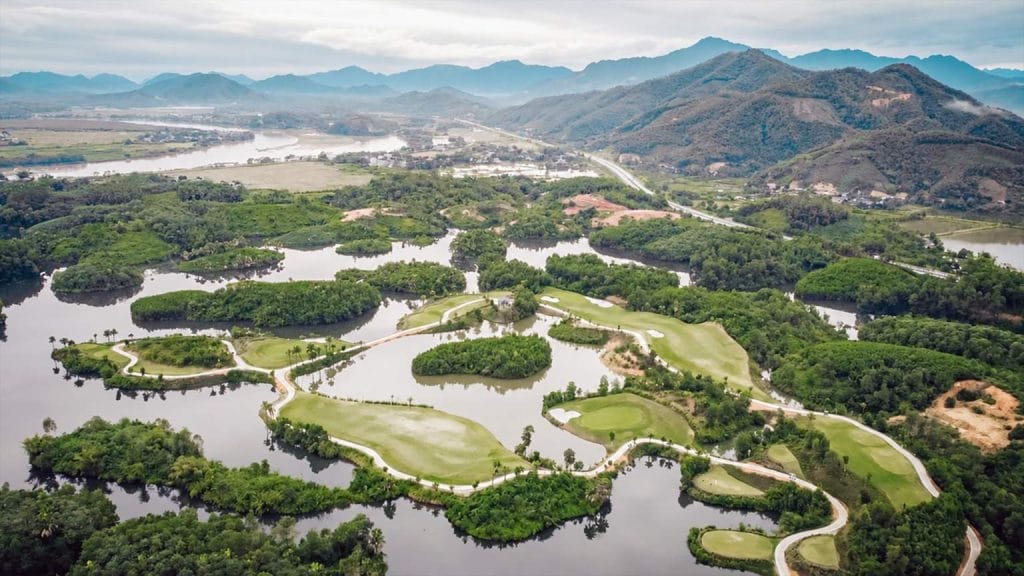 Aerial view of Yen Bai Star Golf & Resort holes wrapped around Minh Quan Lake, with mountains behind