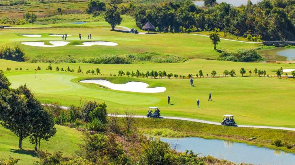 Golfers and carts beside a bunkered green on a sunny day in Da Lat, Vietnam