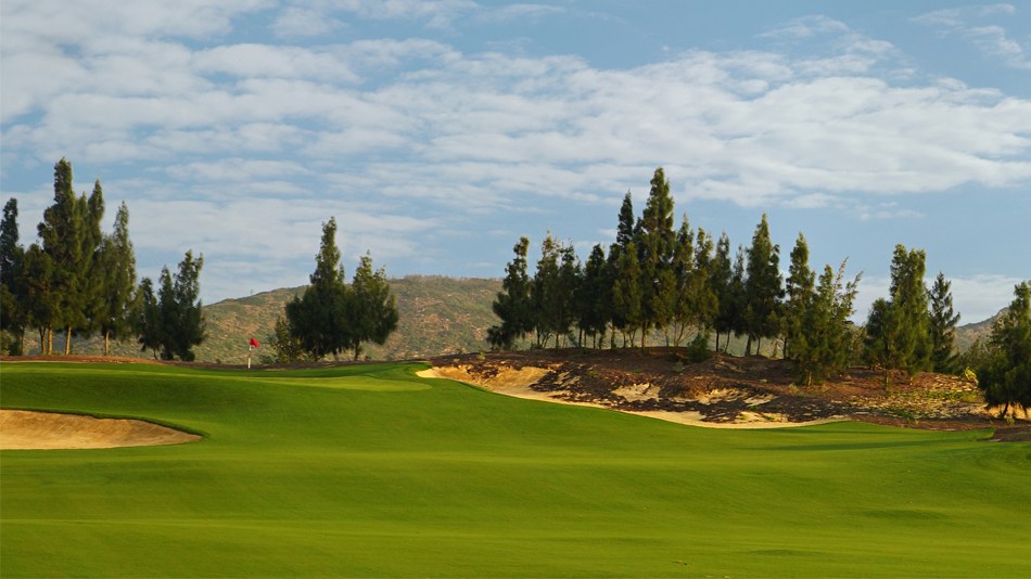 10th hole of the FLC Quy Nhon Mountain Course with pine trees and a greenside bunker