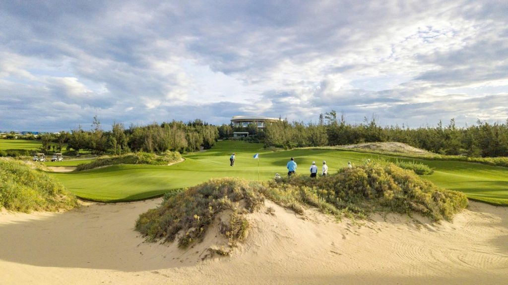 Fairway of the FLC Quy Nhon Ocean Course with flowers in front and mountains and the sea behind
