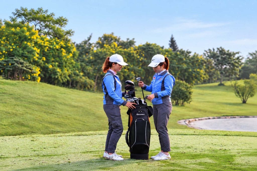 Two caddies sorting clubs in a golf bag on the tee before a round near Hanoi