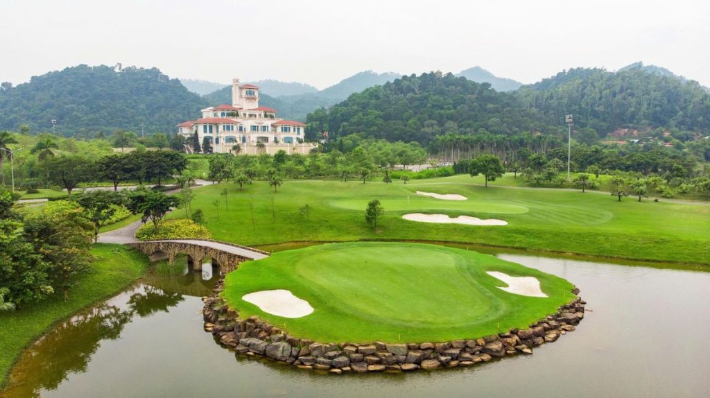 Island green with stone bridge and the clubhouse behind at BRG Legend Hill Golf Resort near Noi Bai Airport, Hanoi