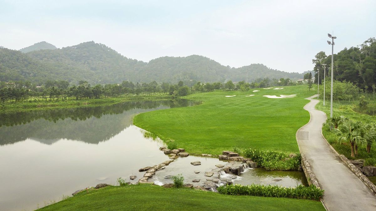 Lakeside fairway with floodlight towers and cart path at BRG Legend Hill Golf Resort, Hanoi