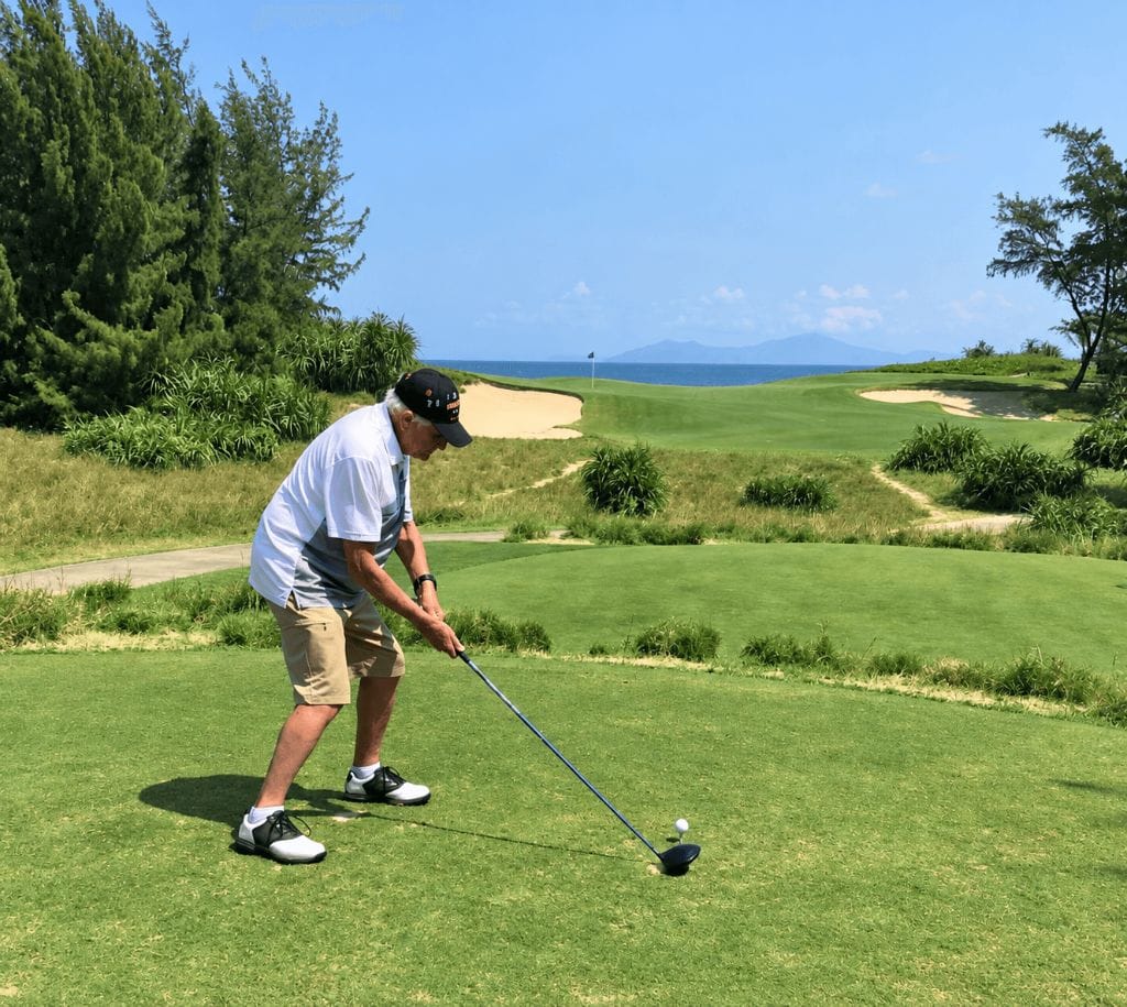 Senior golfer addressing the ball on a tee box, with the fairway and bunkers ahead
