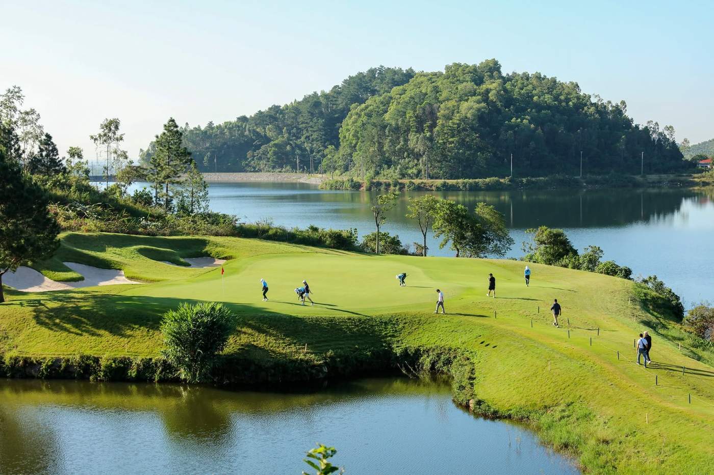 Lakeside hole with bunkers and forested hills at Thanh Lanh Valley Golf Resort, a Nick Faldo design